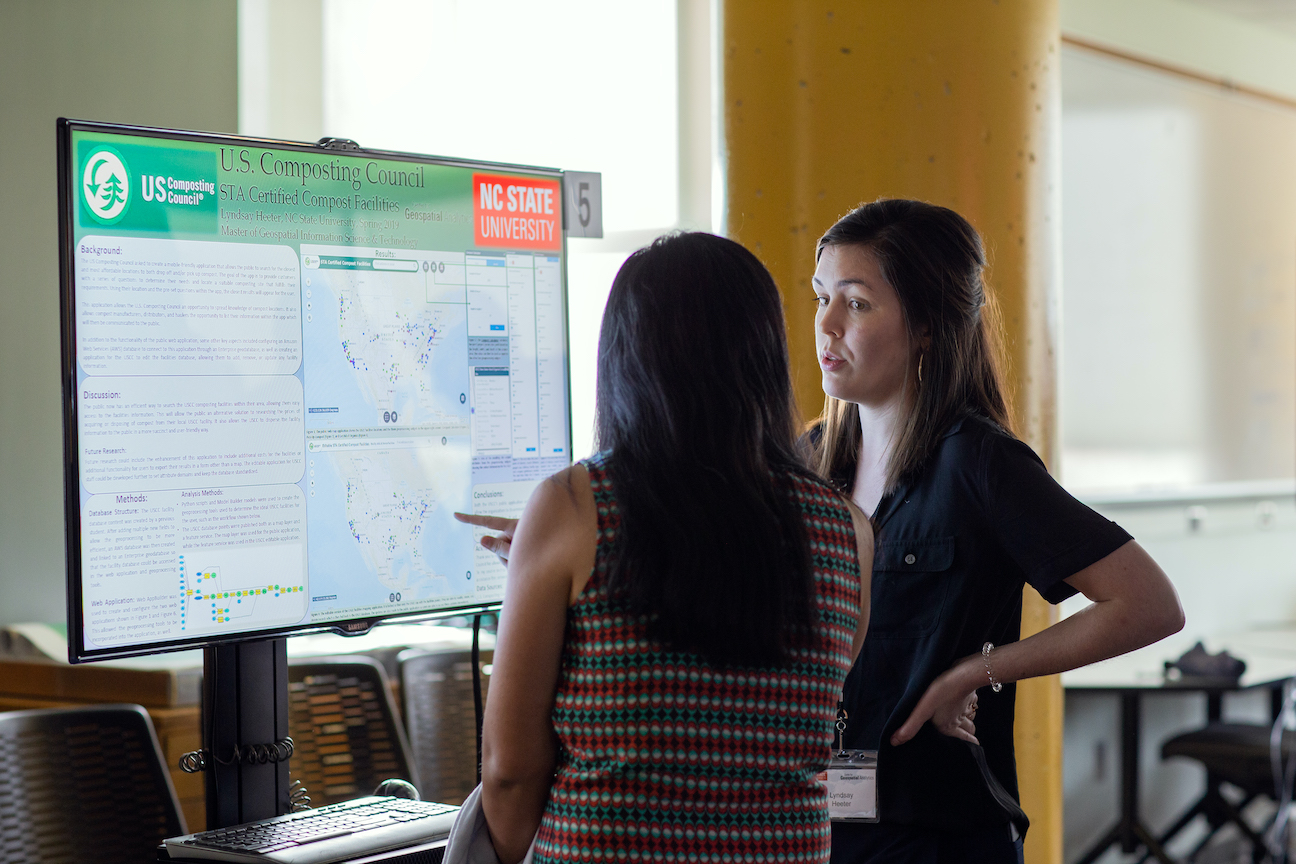 Two researchers discuss maps shown on a screen.