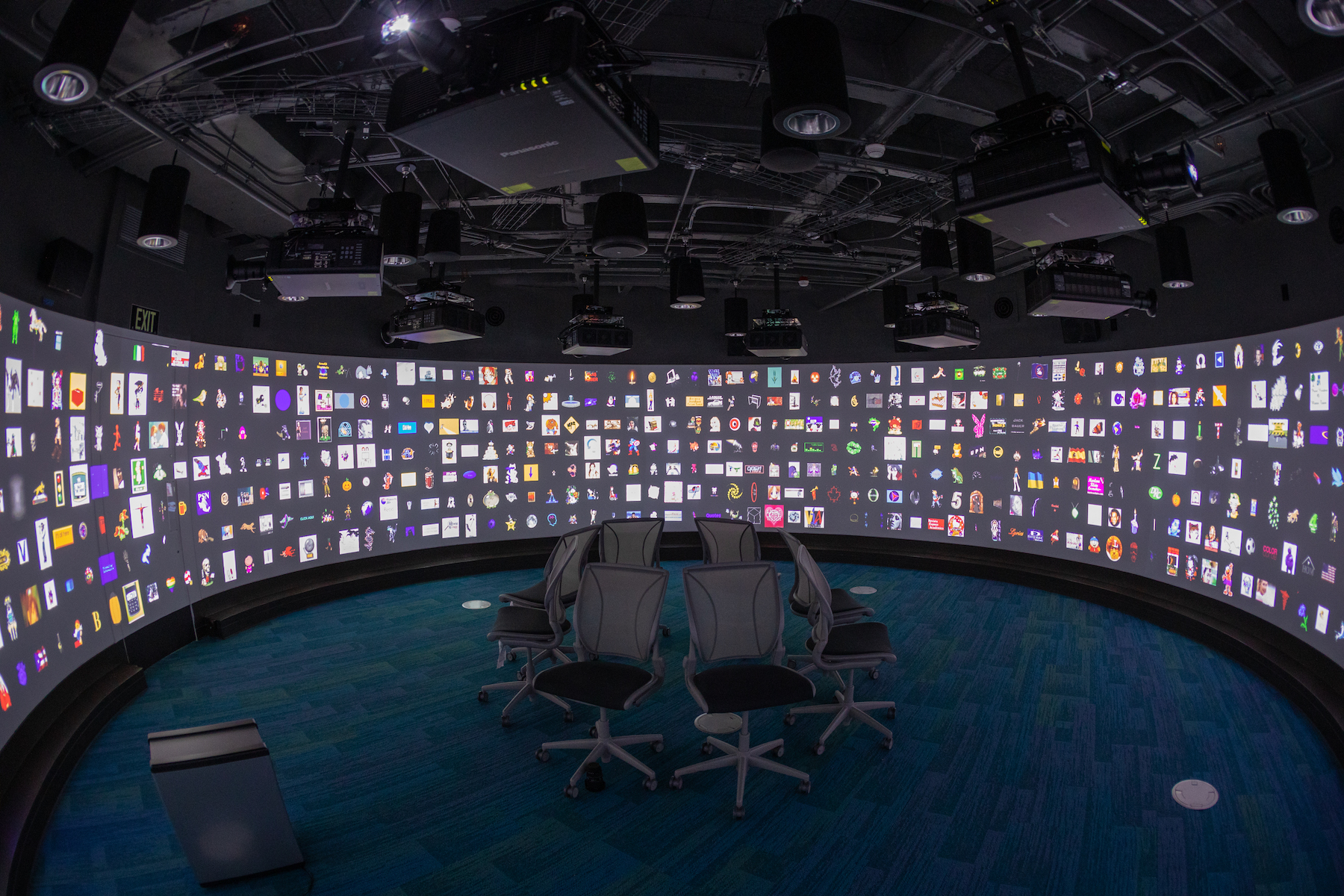 large curved projection screen displaying multiple squares with a variety of shapes and colors. 6 chairs in a circle in the center