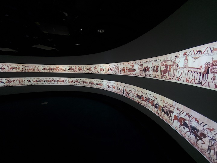 Projection of the Bayeux tapestry depicting a battle with human figures and horses
