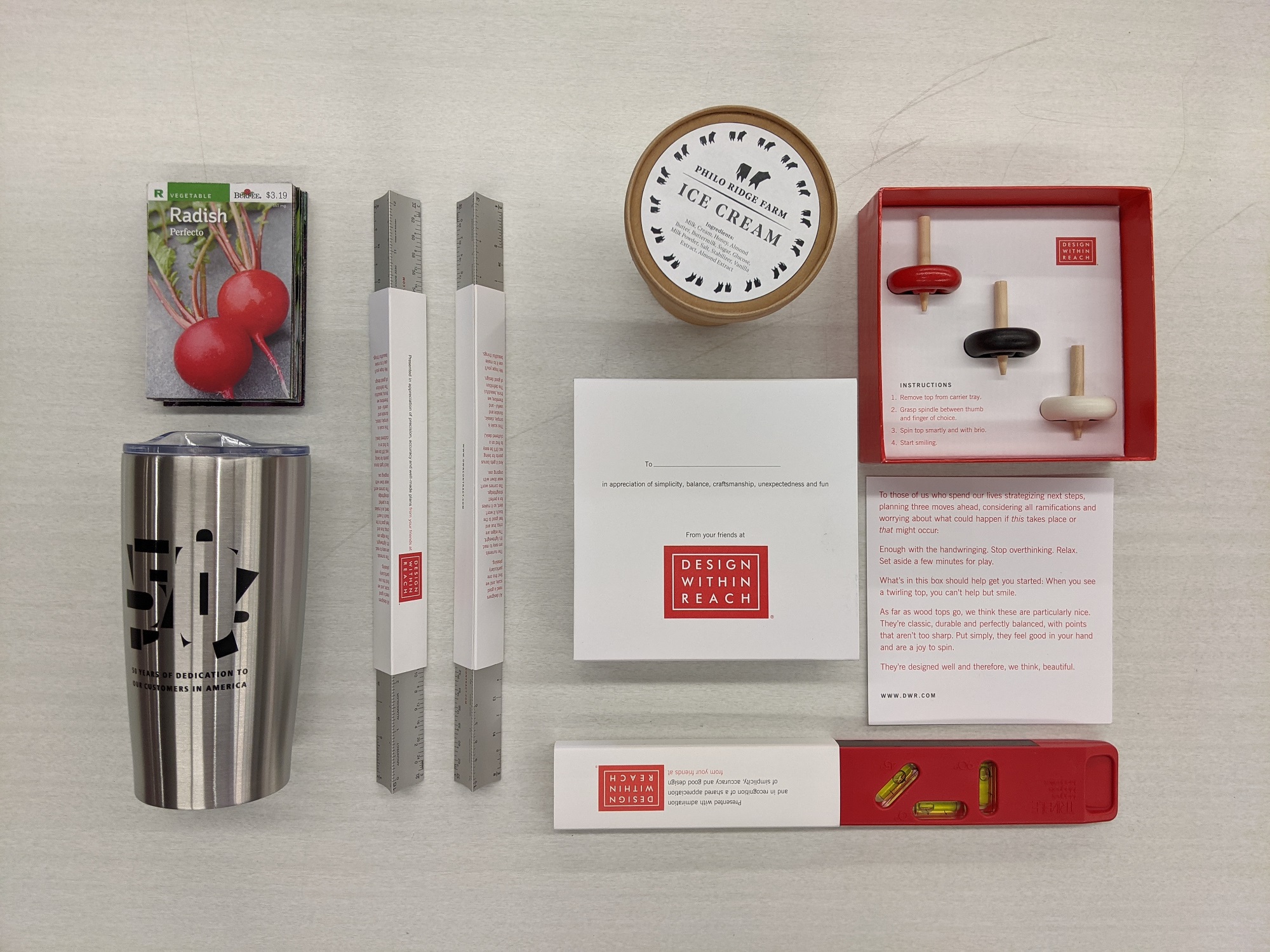 A variety of objects on a table, including a thermos, rulers, levels, radish seeds, an ice cream container, and tops.