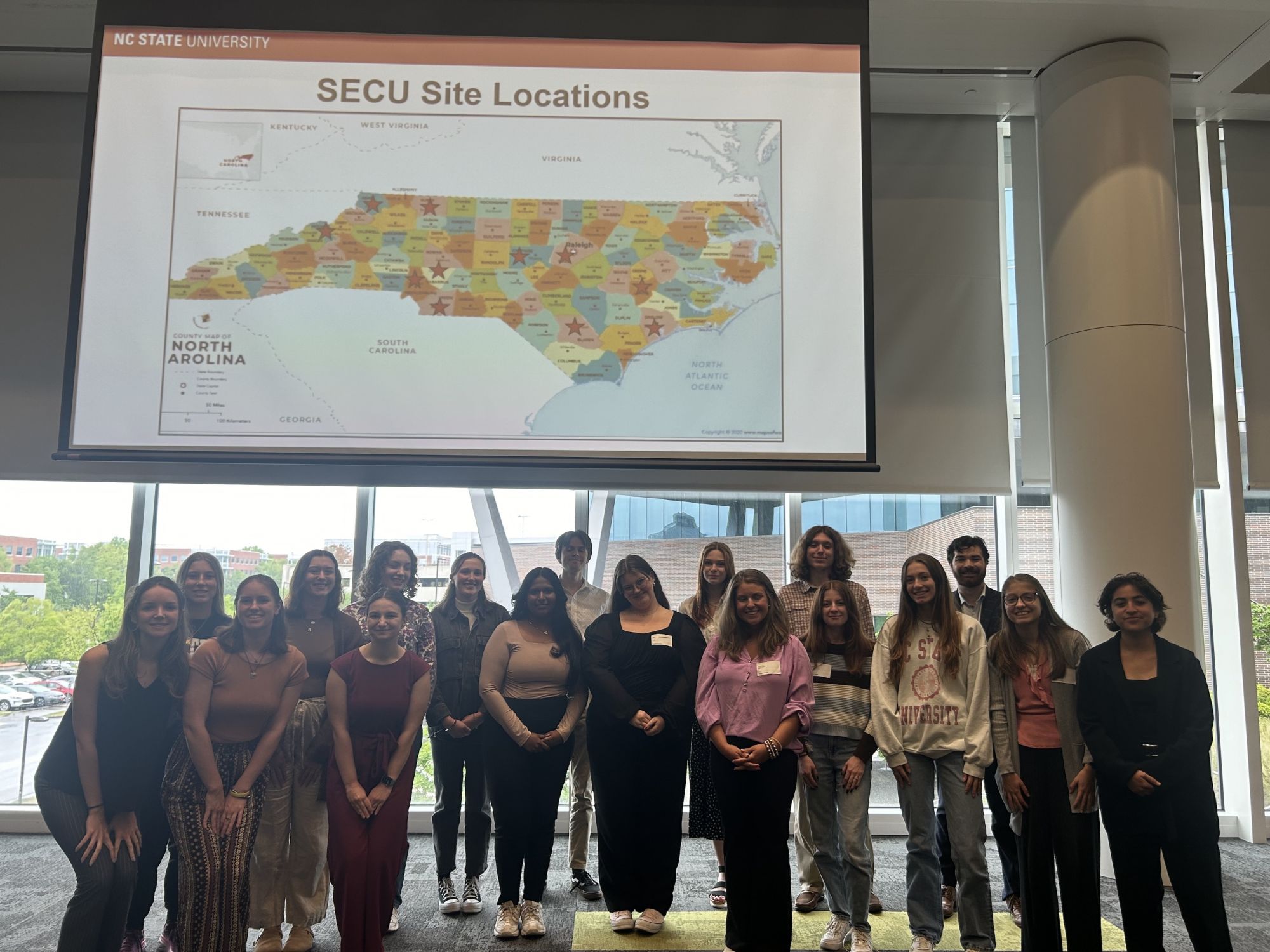 Students standing in front of a map of North Carolina, that says "SECU Site Locations."