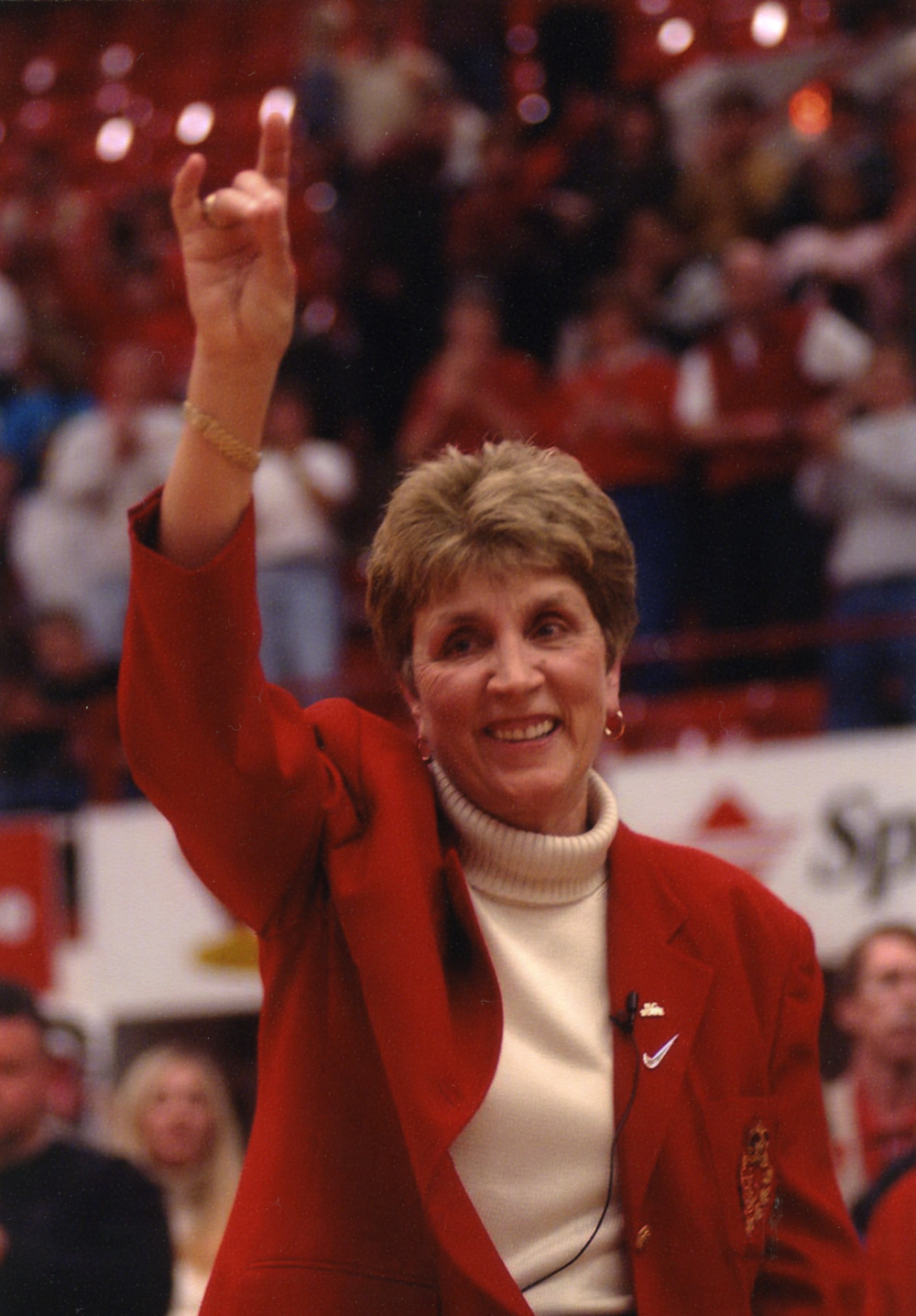 Color photo of women's basketball coach Kay Yow making the wolf symbol at a women's basketball game.