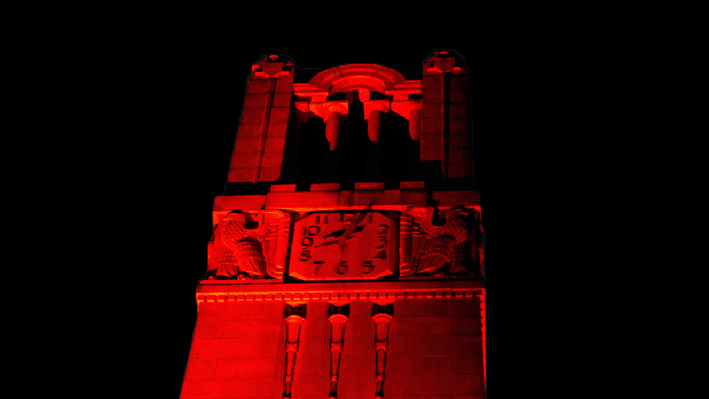 Color image of the Memorial Bell Tower lit up in red light against a black background.