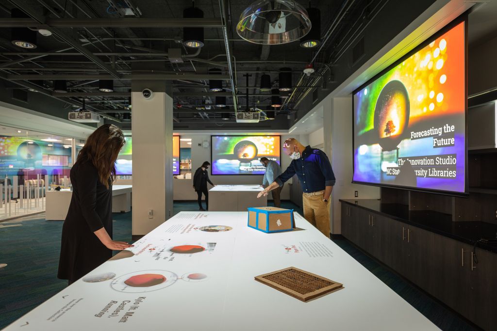 The Innovation Studio is shown: people interact with digital content projected onto the tables. Colorful graphics are projected on screens in the background.