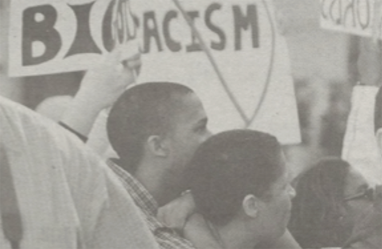 Black and white image of students marching with signs demanding end to racism on campus.