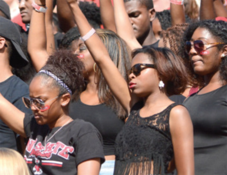 Black student with arms raised protesting during the National Anthem