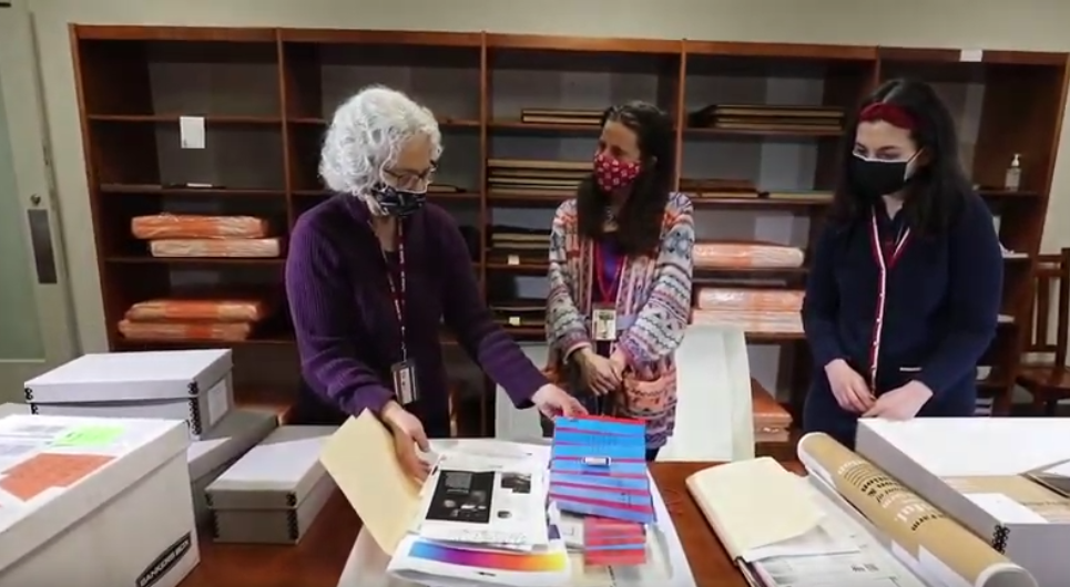 Three women stand in front of a table covered in folders, papers, and boxes from the special collections.