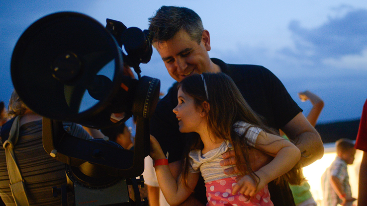 Father and daughter looking through telescope.