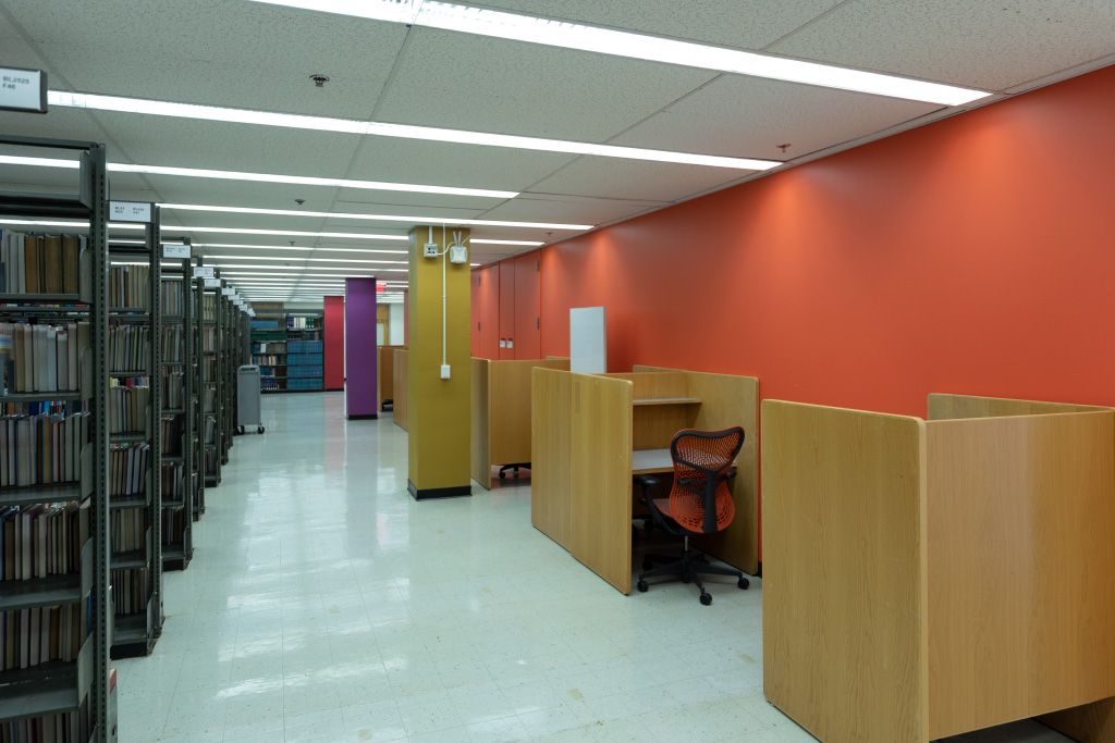 Full floor to ceiling bookshelves and individual carrel seating with task chairs along orange wall.