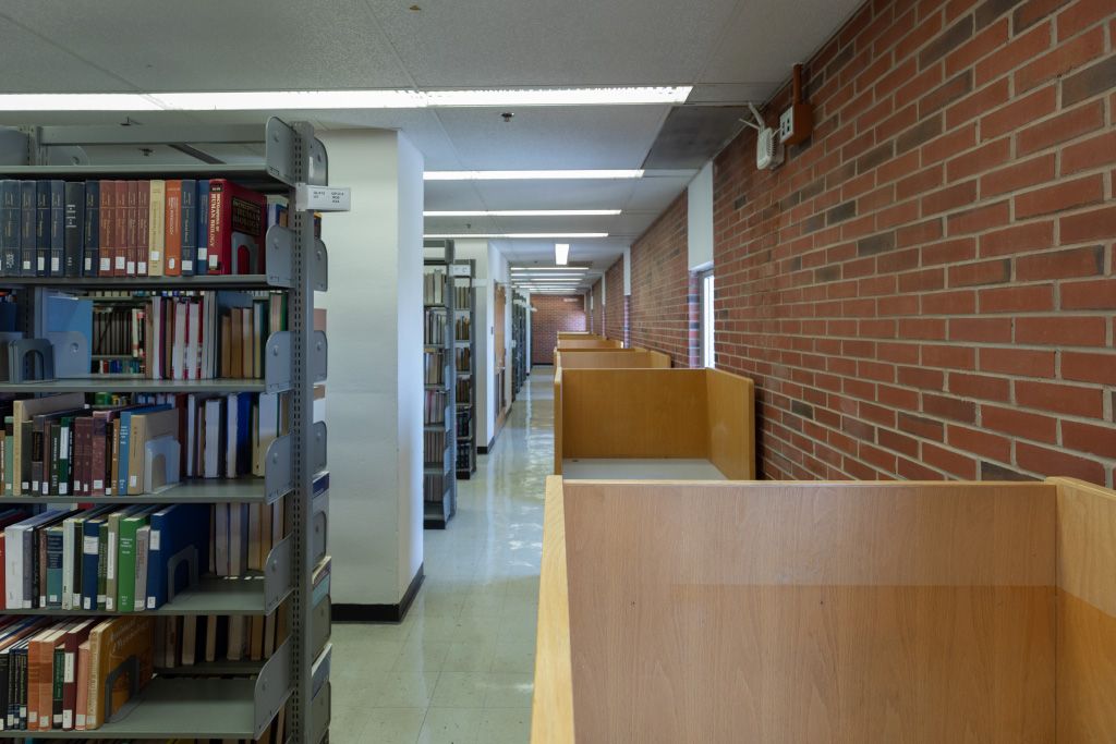 Individual carrels with moulded chairs along a brick wall across the aisle from floor to ceiling bookshelves.