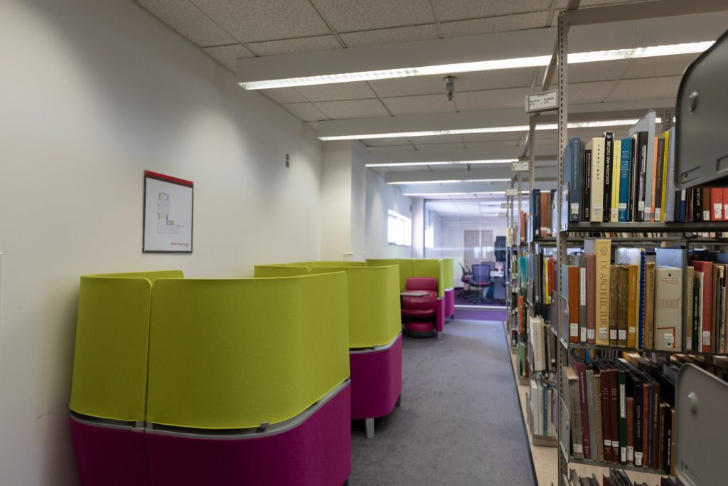 Row of Brody carrels with integrated seat, desk, foot stool, and privacy panels across the aisle from bookshelves.
