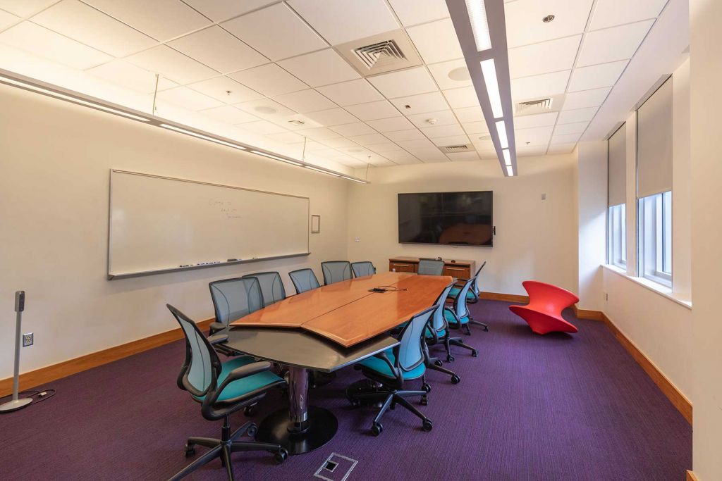 Study room with large table surrounded by twelve chairs, wall-mounted whiteboard, wall-mounted display, and exterior windows