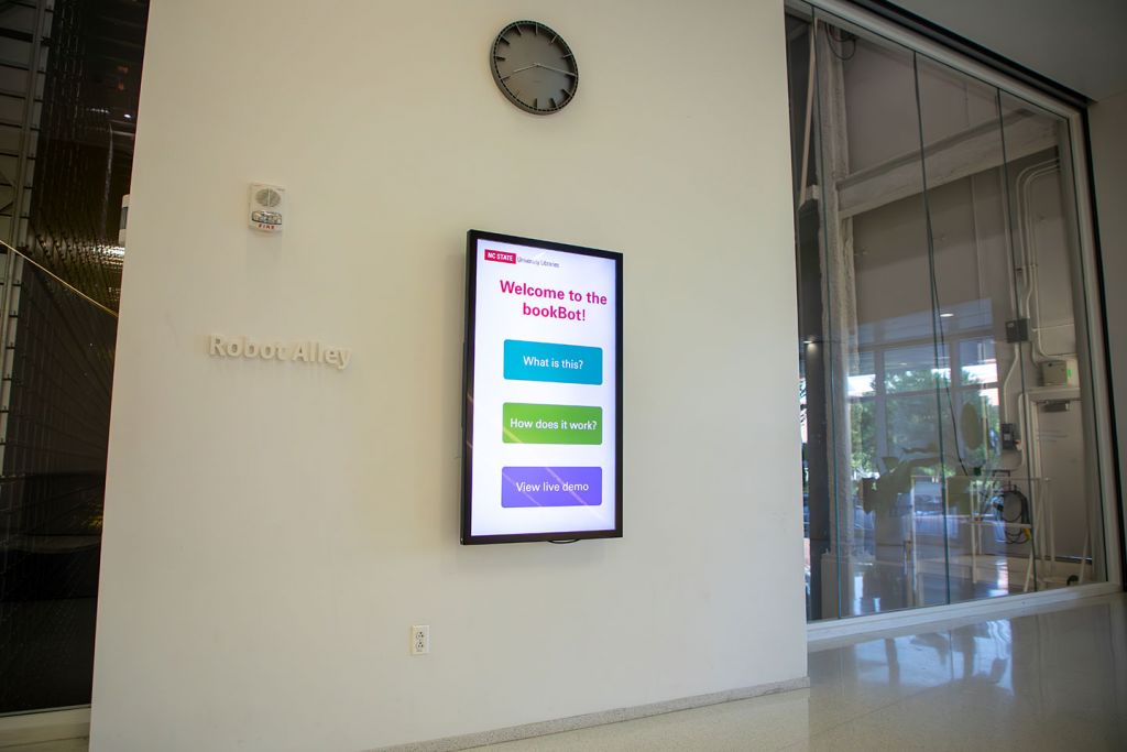 Large touchscreen mounted on wall next to large windows overlooking the bookBot.