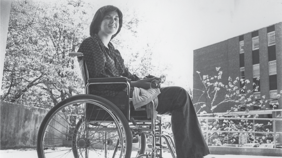 Black and white photo of student in a wheelchair on campus