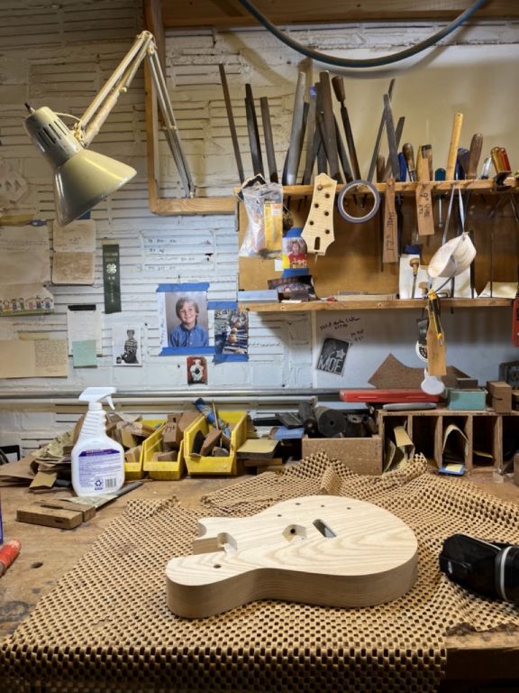 Guitar workshop desk with tools, an unfinished guitar, and other personal items