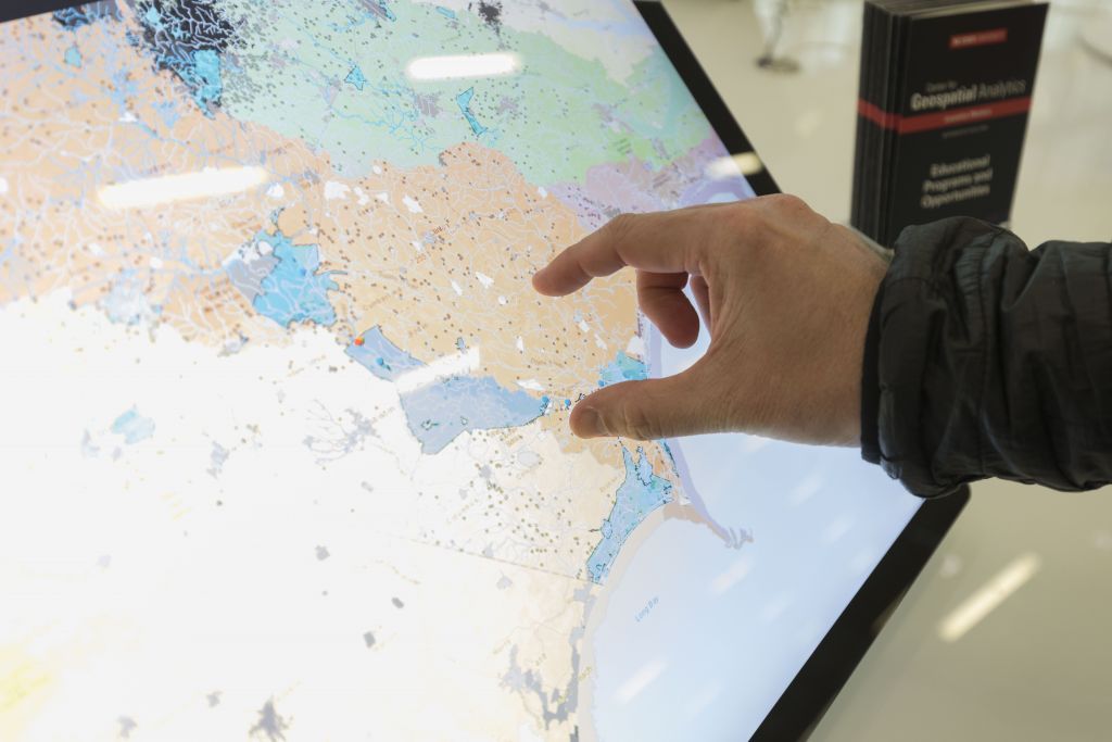 A hand interacts with a large screen showing a map of the North Carolina coast