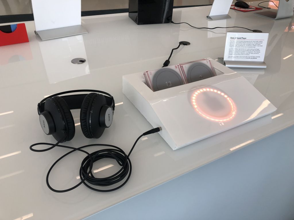 A white device with a glowing circle connected to headphones