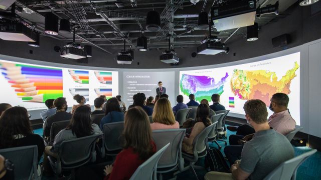 A large audience watches a presentation with colorful graphics