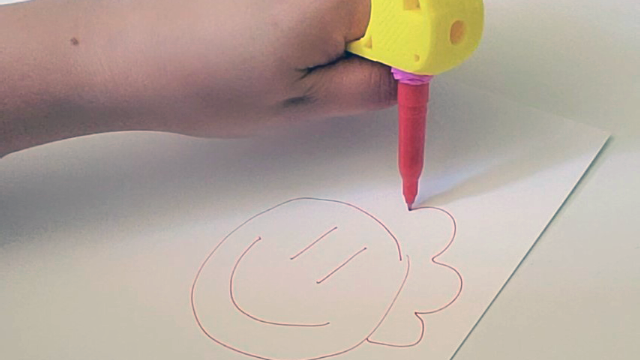 A hand drawing a smiley face with an assistive device