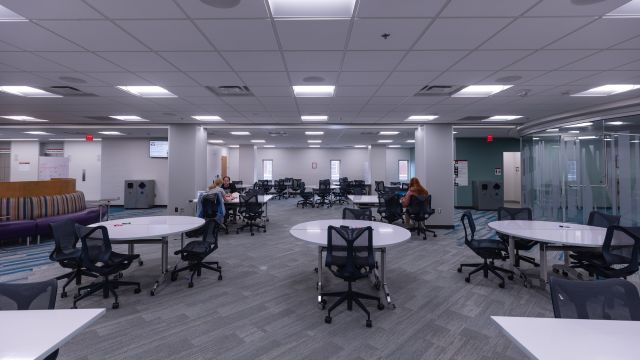 A large space with around ten big tables and office chairs