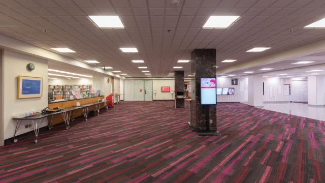 Side view of the Ask Us Lobby showing the information eboard on a column and touchscreens on the walls in the background.