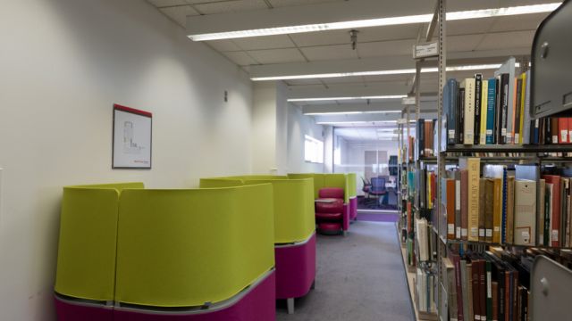 Row of Brody carrels with integrated seat, desk, foot stool, and privacy panels across the aisle from bookshelves.