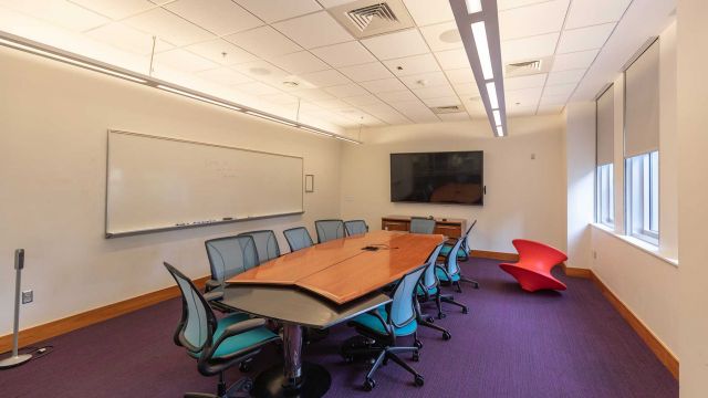Study room with large table surrounded by twelve chairs, wall-mounted whiteboard, wall-mounted display, and exterior windows