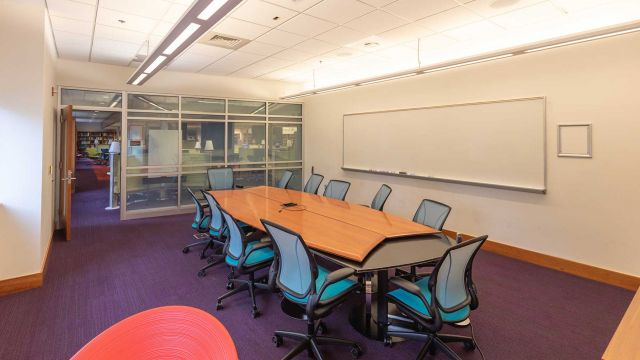 Study room with large table surrounded by twelve chairs, wall-mounted whiteboard, and glass entrance wall