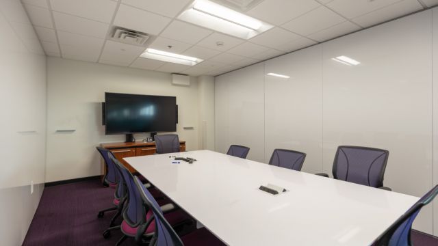 Large study room with conference table, task chairs, large display, and whiteboard walls.