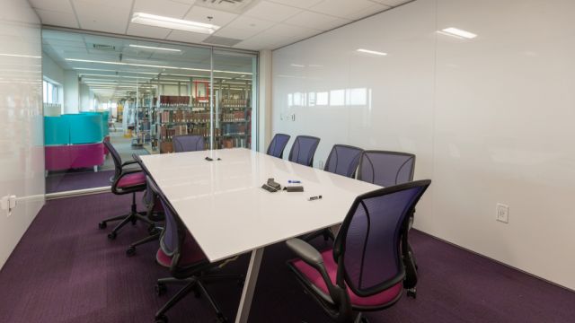 Large study room with conference table, task chairs, glass entrance wall, and whiteboard walls.