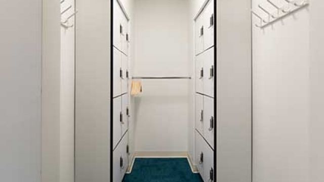 Locker cubby with sixteen small lockers with keypad lock, wall-mounted hooks, and rail with hangers.