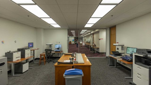 Room with printers, book scanners, and computers on adjustable height desks with central cabinet storage