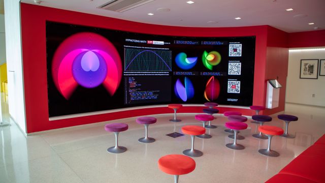 Stools in front of the large, curved screen of the Immersion Theater. The screen shows visuals from an exhibit called 