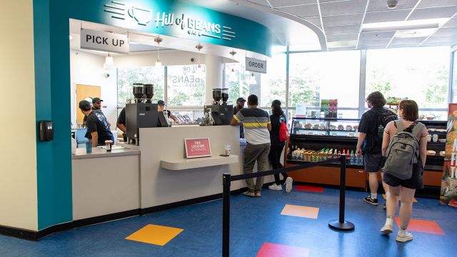 Hill of Beans Café counter serving guests with coolers holding food and large exterior windows in the background