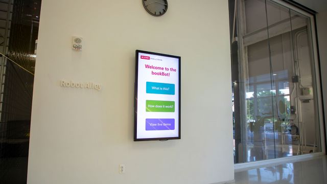 Large touchscreen mounted on wall next to large windows overlooking the bookBot.