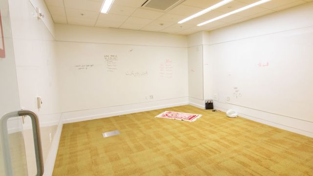 Open room with yellow carpet, whiteboard walls, and prayer rug.