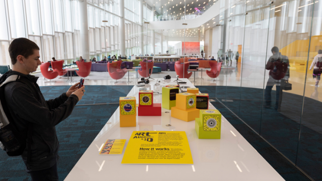 Brightly colored blocks with QR codes are displayed on a table, and a man aims a smartphone at one of them