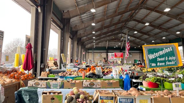 In a large, open-air warehouse, tables are laden with produce