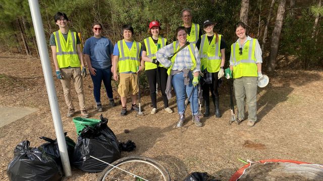 an image of the group of staff members wearing yellow vests posing in front of various trash items and bags collected