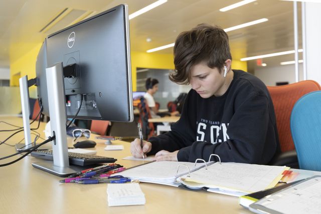 Student working at a computer workstation with dual monitors and enough space on the desk for paper notes