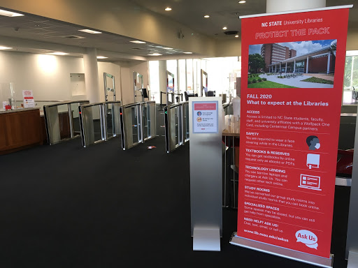 Two physical signs at the Libraries with information about safety requirements and what to expect when visiting during Fall 2020.