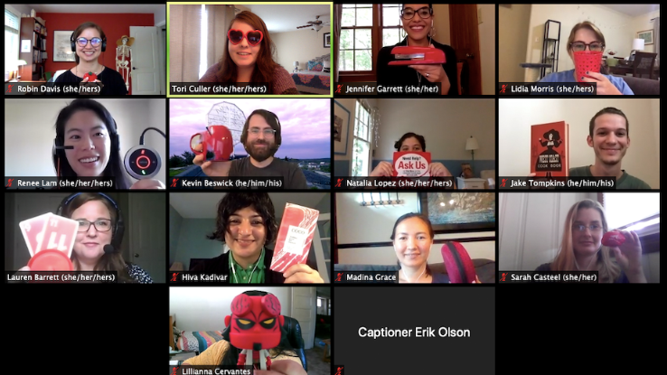 Zoom screenshot of thirteen happy people, each holding up a red object